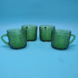 May include: Set of four green glass mugs with a textured surface. The mugs have a rounded shape and a handle on one side.