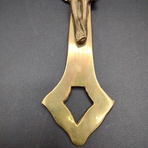 K&ouml;nnte beinhalten: Ein goldfarbenes Metallkreuz mit einer detaillierten Figur von Jesus Christus. Das Kreuz hat ein dekoratives, verziertes Design mit einer rautenf&ouml;rmigen &Ouml;ffnung am unteren Ende.