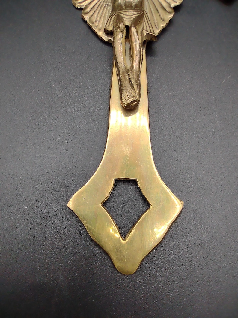 K&ouml;nnte beinhalten: Ein goldfarbenes Metallkreuz mit einer detaillierten Figur von Jesus Christus. Das Kreuz hat ein dekoratives, verziertes Design mit einer rautenf&ouml;rmigen &Ouml;ffnung am unteren Ende.