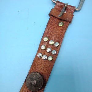 Peut inclure: Une ceinture en cuir marron avec une boucle argent&eacute;e et des clous m&eacute;talliques. La ceinture a une pi&egrave;ce d&eacute;corative ronde en m&eacute;tal avec un motif d'&eacute;toile.