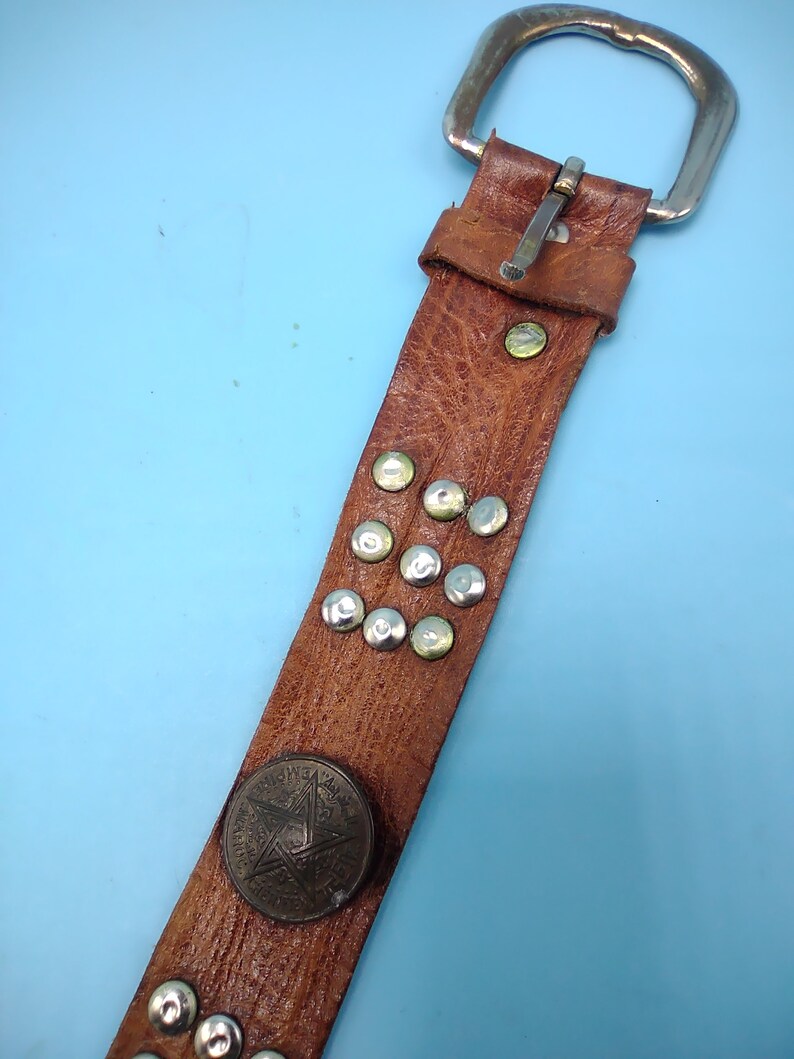 Peut inclure: Une ceinture en cuir marron avec une boucle argent&eacute;e et des clous m&eacute;talliques. La ceinture a une pi&egrave;ce d&eacute;corative ronde en m&eacute;tal avec un motif d'&eacute;toile.
