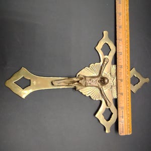 K&ouml;nnte beinhalten: Ein goldfarbenes Metallkreuz mit einer detaillierten Figur von Jesus Christus. Das Kreuz hat ein dekoratives Design mit einem Sonnenstrahlenmuster hinter der Figur.