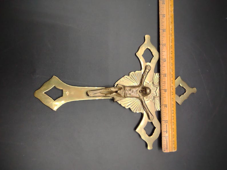 K&ouml;nnte beinhalten: Ein goldfarbenes Metallkreuz mit einer detaillierten Figur von Jesus Christus. Das Kreuz hat ein dekoratives Design mit einem Sonnenstrahlenmuster hinter der Figur.