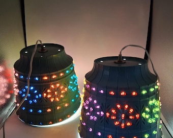 May include: Two bell-shaped blue plastic light fixtures featuring embossed floral patterns and numerous small, multi-colored LED lights in shades of orange, blue, green, and purple. Each fixture has a white power cord extending from the top center.