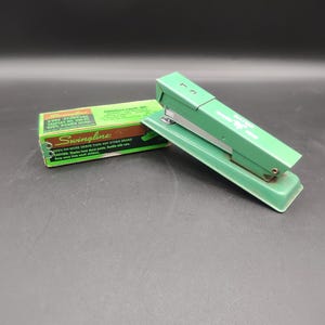 May include: A green Swingline stapler with a box of staples. The box says "Swingline" and "1000 Standard Staples 1/2 in. 26/6  100% Round Wire".