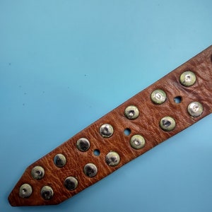 Peut inclure: Une ceinture en cuir marron avec des clous argent&eacute;s. La ceinture est sur un fond bleu clair.