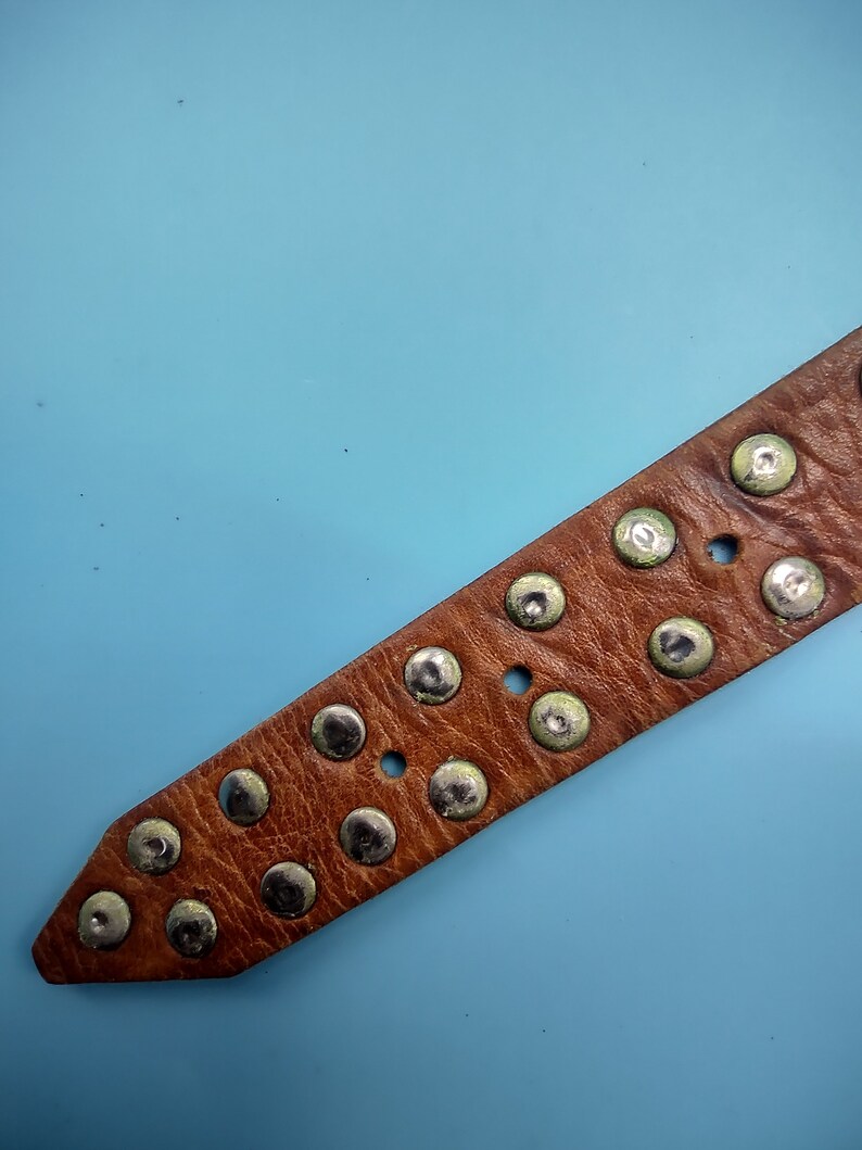 Peut inclure: Une ceinture en cuir marron avec des clous argent&eacute;s. La ceinture est sur un fond bleu clair.