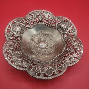 May include: A silver, decorative bowl with an intricate floral design. The bowl has a scalloped edge and a raised center.