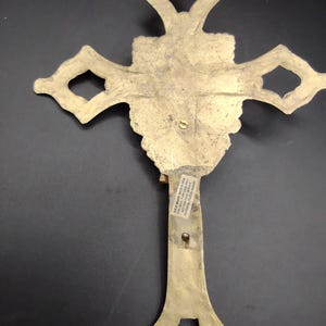 K&ouml;nnte beinhalten: Ein goldfarbenes Metallkreuz mit einem verzierten Design. Auf der R&uuml;ckseite des Kreuzes befindet sich ein Aufkleber mit der Aufschrift "Brass Made in India For Decorative Purposes Only Not for Religious Use Potential Lead Hazard"