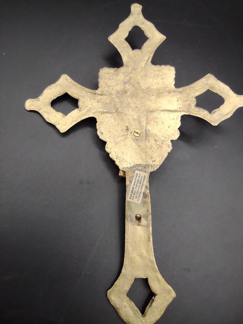 K&ouml;nnte beinhalten: Ein goldfarbenes Metallkreuz mit einem verzierten Design. Auf der R&uuml;ckseite des Kreuzes befindet sich ein Aufkleber mit der Aufschrift "Brass Made in India For Decorative Purposes Only Not for Religious Use Potential Lead Hazard"