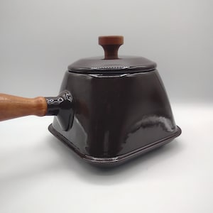 May include: A dark brown enamel saucepan with a wooden handle and lid. The saucepan has a square shape and a glossy finish.