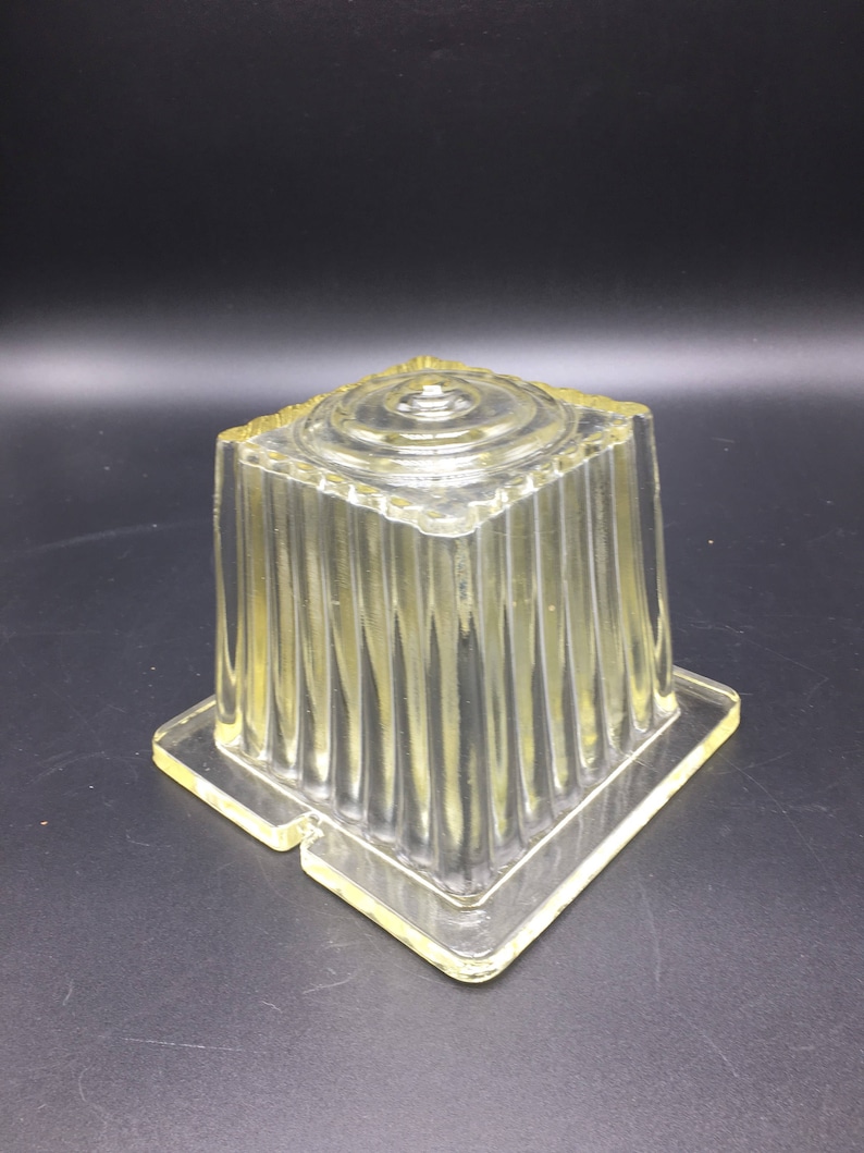 May include: A clear glass mold with a square base and a fluted design. The mold is designed for making gelatin desserts.