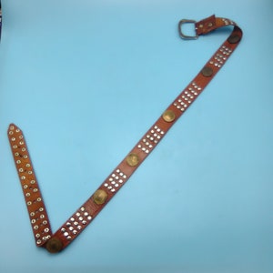 Peut inclure: Une ceinture en cuir marron avec des clous argent&eacute;s et des accents ronds dor&eacute;s. La ceinture a une boucle argent&eacute;e.
