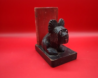 May include: A black wooden bookend shaped like a sitting dog. The bookend has a rectangular base and a red book is visible behind the dog.