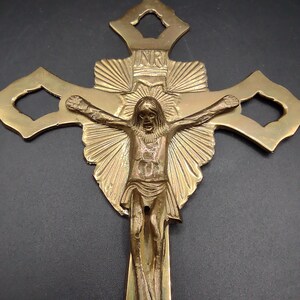 K&ouml;nnte beinhalten: Ein goldfarbenes Messingkreuz mit einer detaillierten Darstellung von Jesus Christus am Kreuz. Das Kreuz hat ein dekoratives Design mit einem Sonnenstrahlenmuster und den Buchstaben "INR" oben.