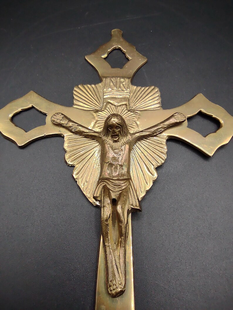 K&ouml;nnte beinhalten: Ein goldfarbenes Messingkreuz mit einer detaillierten Darstellung von Jesus Christus am Kreuz. Das Kreuz hat ein dekoratives Design mit einem Sonnenstrahlenmuster und den Buchstaben "INR" oben.