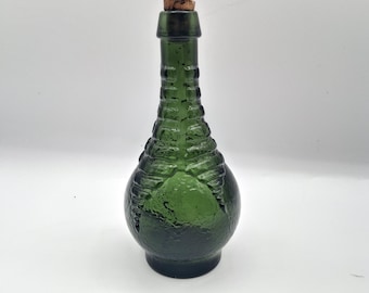 May include: A dark green glass bottle with a rounded base and a long, slender neck. The exterior features a textured, raised pattern resembling skeletal ribs or claw-like ridges extending from the neck down to the body. A small cork stopper is inserted into the top opening of the bottle.