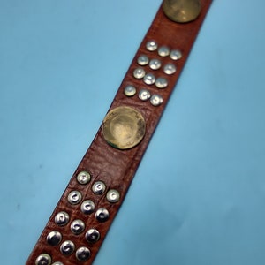 Peut inclure: Une ceinture en cuir marron avec des clous argent&eacute;s et des accents circulaires dor&eacute;s.