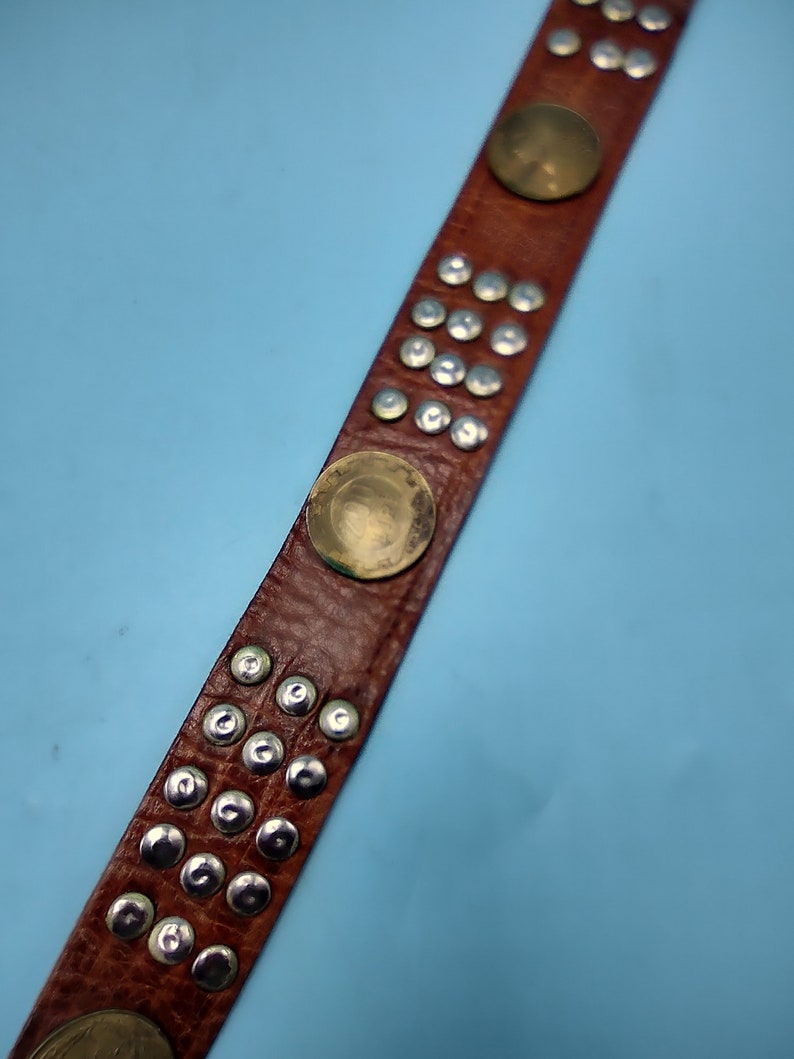 Peut inclure: Une ceinture en cuir marron avec des clous argent&eacute;s et des accents circulaires dor&eacute;s.