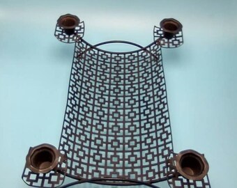 May include: A black metal candle holder with a geometric design and four candle cups. The candle holder is on a light blue background.