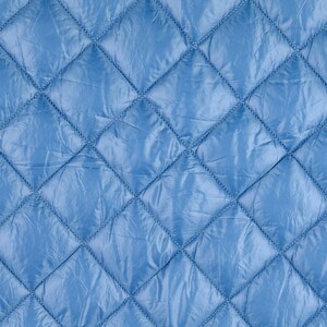 Könnte beinhalten: Nahaufnahme eines blauen gesteppten Stoffes mit rautenförmigen Nähten. Der Stoff hat eine glatte, glänzende Oberfläche.