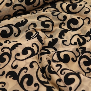 Può includere: Tessuto beige trasparente con un motivo floreale nero. Il tessuto è testurizzato e ha un aspetto delicato, quasi come pizzo.