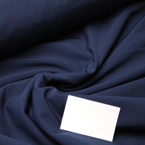 Op de afbeelding: Een close-up van een donkerblauwe stof met een witte kaart erop. De stof is gevouwen en heeft een zachte, gladde textuur.