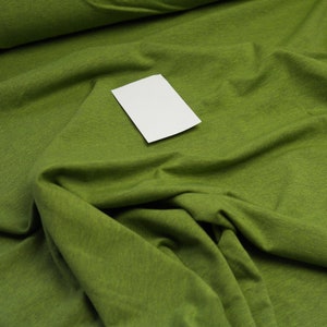 Può includere: Primo piano di un tessuto verde con un cartoncino bianco sopra. Il tessuto ha una superficie testurizzata ed è piegato in modo da creare un aspetto morbido e invitante.