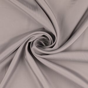 Può includere: Primo piano di un tessuto liscio di colore grigio con una texture morbida e fluida. Il tessuto è drappeggiato e piegato, creando un motivo a spirale.