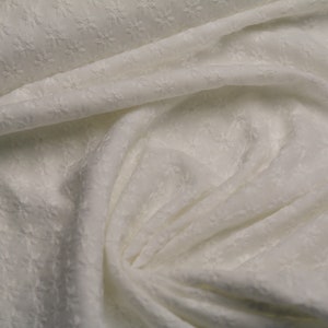 Pode incluir: Tecido branco com um padrão floral texturizado e em relevo. O tecido é macio e cai bem.