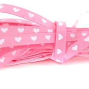 Op de afbeelding: Roze lint met witte hartjesprint. Het lint is gevouwen en in een knoop geknoopt.
