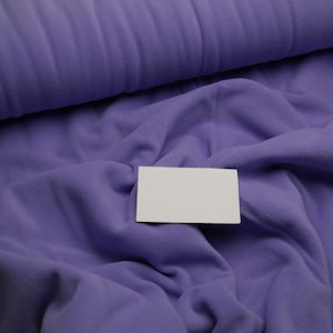 Könnte beinhalten: Ein Nahaufnahme von einem lila Fleece-Stoff mit einer weißen Karte darauf. Der Stoff ist weich und texturiert.
