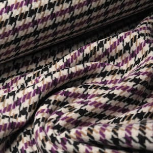 Op de afbeelding: Een close-up van een stof met een ruitpatroon in tinten paars, bruin, zwart en wit.