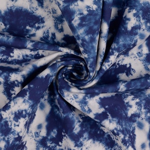 Op de afbeelding: Witte stof met een blauw tie-dye patroon. De stof is gevouwen en gedraaid, waardoor het patroon in detail zichtbaar is.