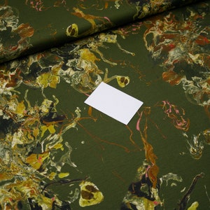 Peut inclure: Tissu vert avec un motif marbré dans des tons de jaune, brun et rose. Le tissu est plié et une carte blanche est placée sur le dessus.