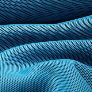 Op de afbeelding: Close-up van een blauwe mesh-stof met een textuur van een honingraatpatroon. De stof is gevouwen en gedrapeerd, waardoor een zachte, vloeiende uitstraling ontstaat.