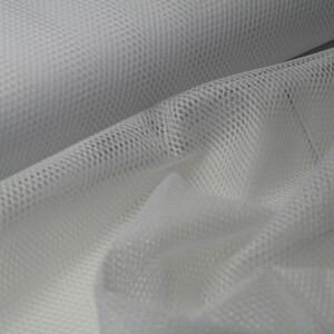 May include: Close-up of white mesh fabric with a honeycomb pattern. The fabric is folded, creating shadows and highlighting the texture. The material appears lightweight and breathable, suitable for various applications.