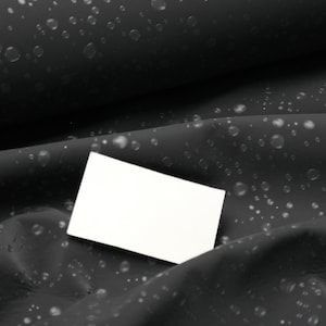 Könnte beinhalten: Eine leere weiße Karte auf einem schwarzen Stoffhintergrund mit einem dezenten Muster aus kleinen weißen Punkten.