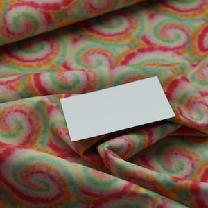 Può includere: Primo piano di un tessuto con un motivo tie-dye in tonalità rosa, giallo e verde. Il tessuto è piegato e un cartoncino bianco è posto sopra.