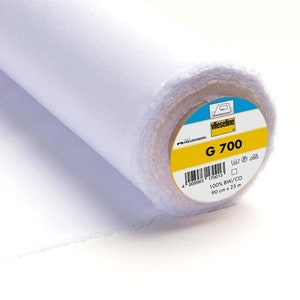 Könnte beinhalten: Eine Rolle weißen Stoffes mit einem Etikett mit der Aufschrift "Vlieseline G 700". Der Stoff ist 90 cm breit und 25 m lang. Das Etikett gibt auch an, dass der Stoff 100% BW/CO ist.