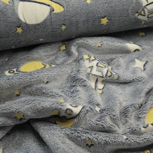 Könnte beinhalten: Grauer Plüschstoff mit Weltraum-Motiv. Das Design umfasst gelbe Planeten, weiße Sterne und ein weiß-gelbes Raumschiff. Der Stoff ist weich und strukturiert, geeignet für Decken oder andere kuschelige Artikel.