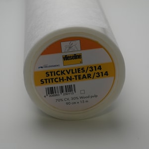 Puede incluir: Un rollo blanco de entretela fusible Vlieseline Stitch-N-Tear, etiquetado como "STICKVLIES/314 STITCH-N-TEAR/314". La etiqueta también indica "70% CV, 30% pulpa de madera" y "90 cm x 15 m".
