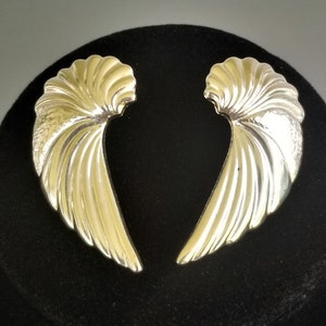 May include: A pair of silver wing-shaped earrings. The earrings are made of a smooth, shiny metal and have a slightly curved shape.