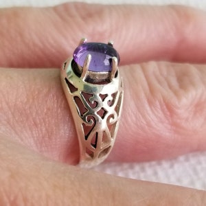 May include: A silver ring with an oval-shaped amethyst gemstone set in a filigree design.