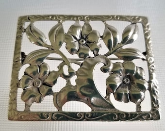 May include: A silver brooch with a floral design. The brooch is made of a delicate, openwork design with flowers and leaves.