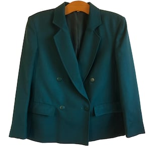 May include: A dark teal double-breasted blazer featuring a notched lapel, long sleeves, and two front flap pockets. The garment is constructed with four matching buttons on the front closure and is displayed on a wooden hanger against a white background.