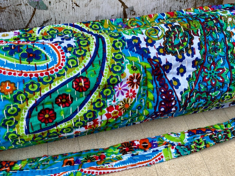 May include: A vibrant yoga mat and strap set, showcasing a paisley pattern in blue, green, red, and white. The design is enhanced with detailed stitching. The strap echoes the mat's colourful design.