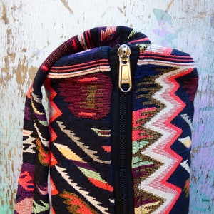 May include: A black yoga mat bag with a zipper closure. The bag is made of a colorful fabric with a geometric pattern in shades of red, pink, white, yellow, green, and blue.