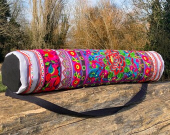 Puede incluir: Una bolsa de yoga colorida con un patrón floral y una correa negra. La bolsa está hecha de tela y tiene un forro blanco.