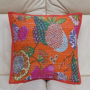 Peut inclure: Coussin carr&eacute; orange avec un motif floral rose, vert, bleu et blanc. Le coussin a une bordure rouge et des coutures blanches. Le coussin est pos&eacute; sur une surface blanche.